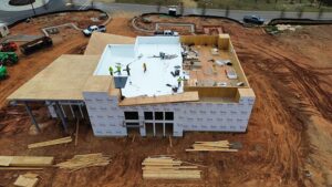 Aerial view of a construction site with a partially built house. Workers in hard hats are installing the roof, considering top roofing colors.