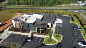 Aerial view of a modern building with a flat roof showcasing top roofing colors, surrounded by trees and grass.