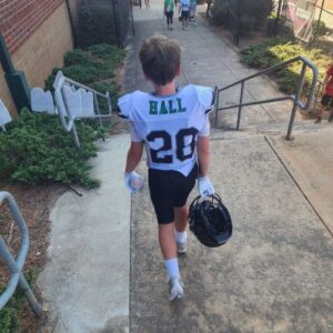 A child walking in a white football Jersey with a name ball and a number 20