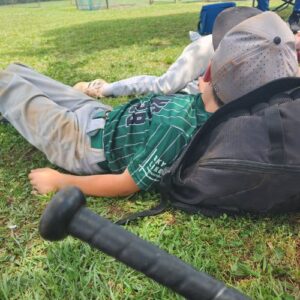 Jr Trojan Baseball player lying on the grass with a bag on his head in Gainesville, GA